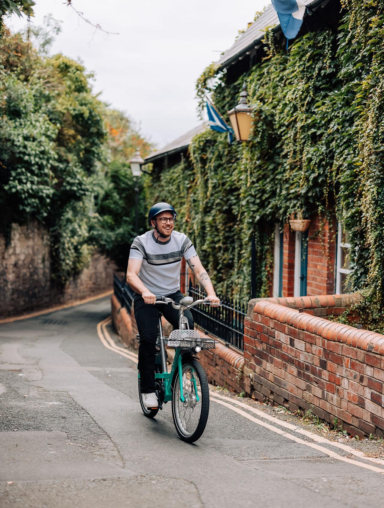 A man in a grey t shirt is smiling and riding a Beryl bike