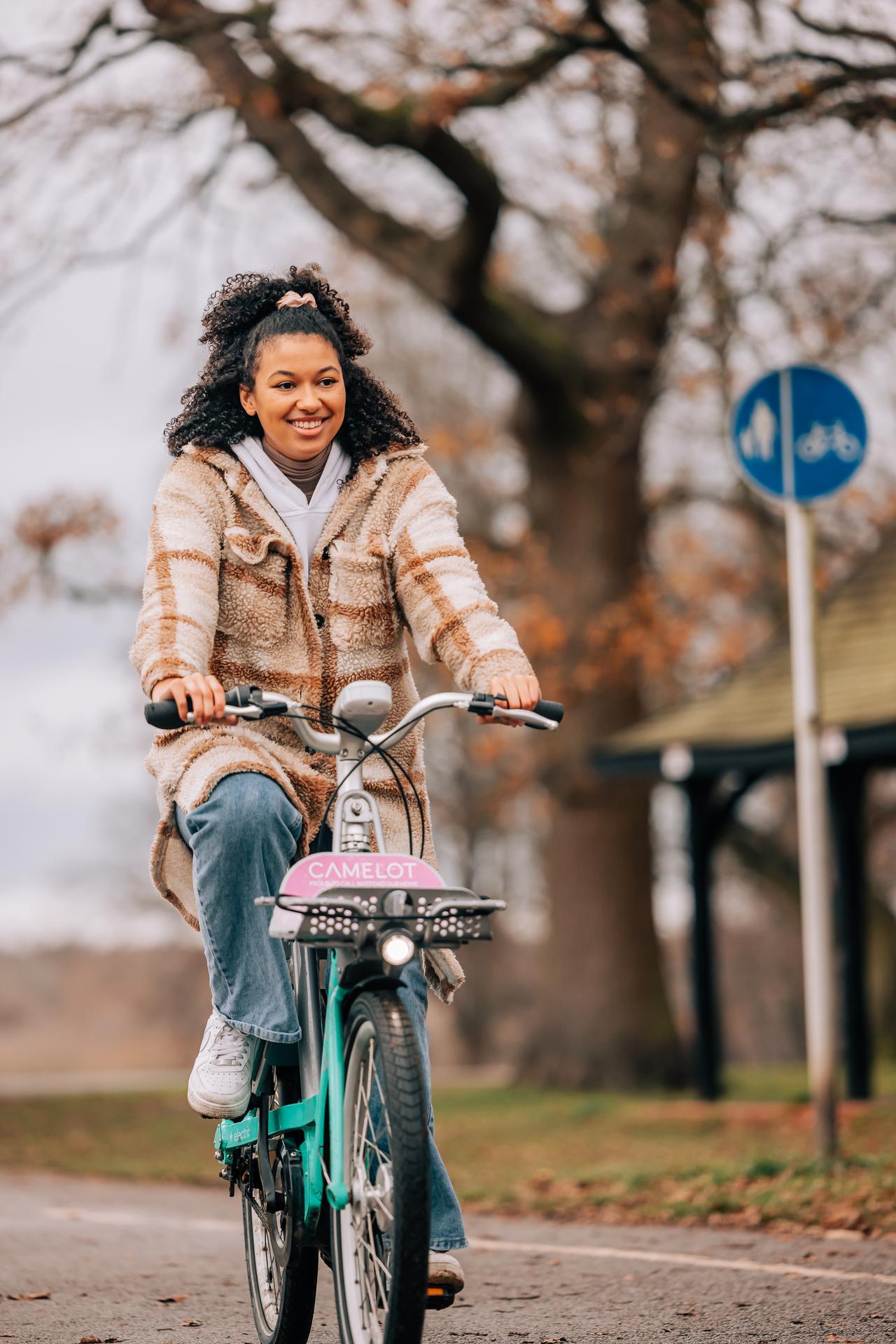 A woman in a checked coat is smiling and riding a Beryl bike