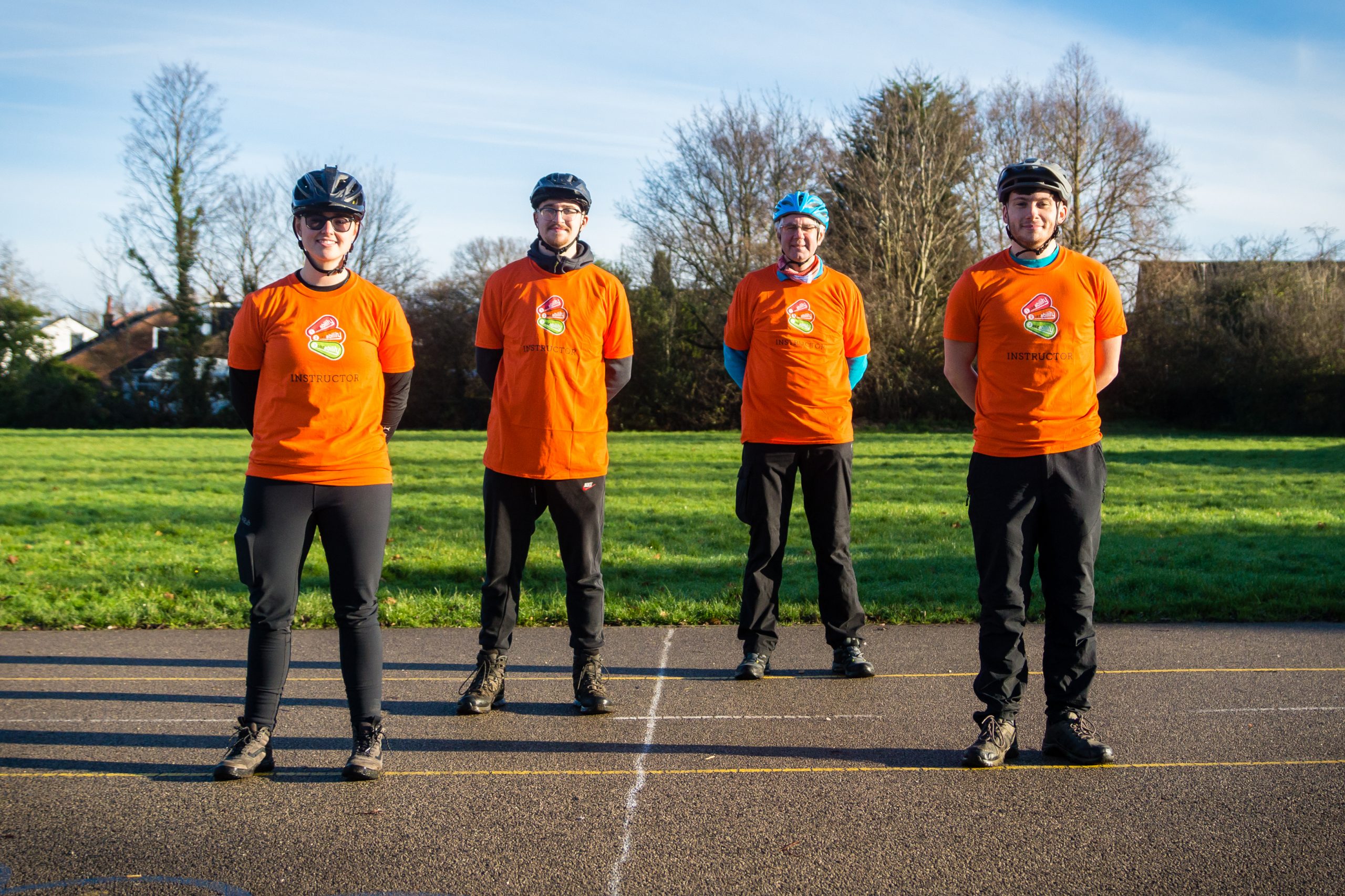 One female and three male Bikeability instructors stood in a line wearing orange t shirts