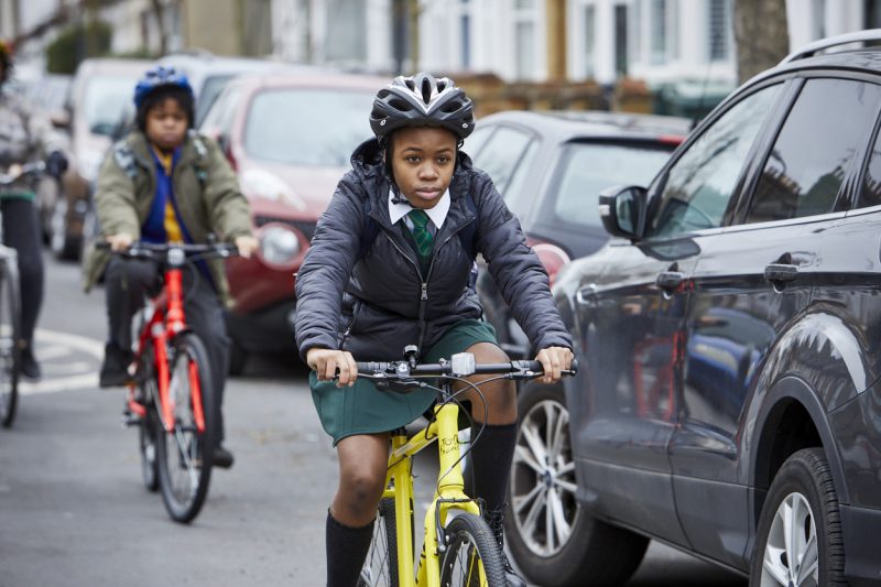 A girl cycles next to a car