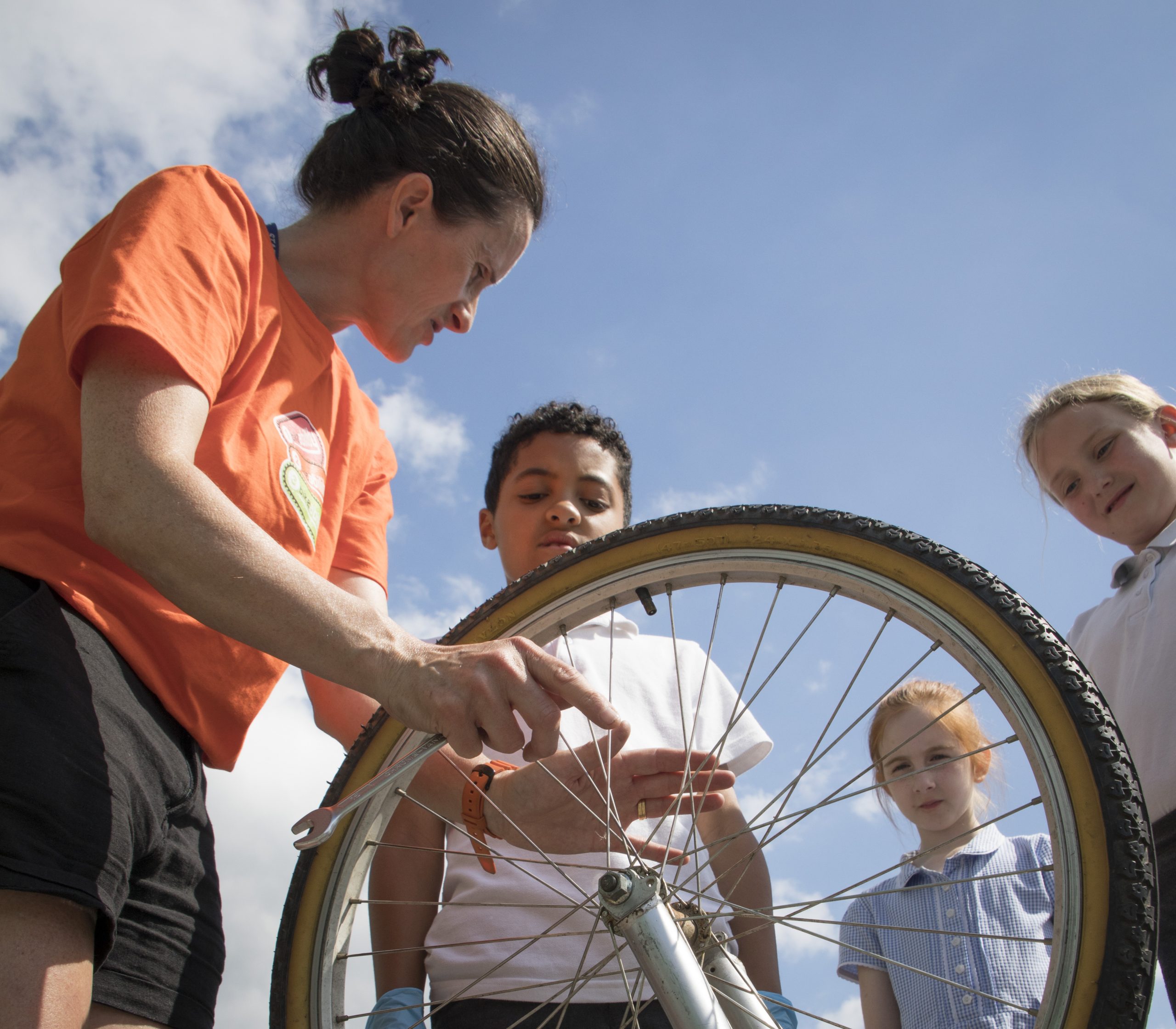 A woman fixes a bike wheel with children looking on