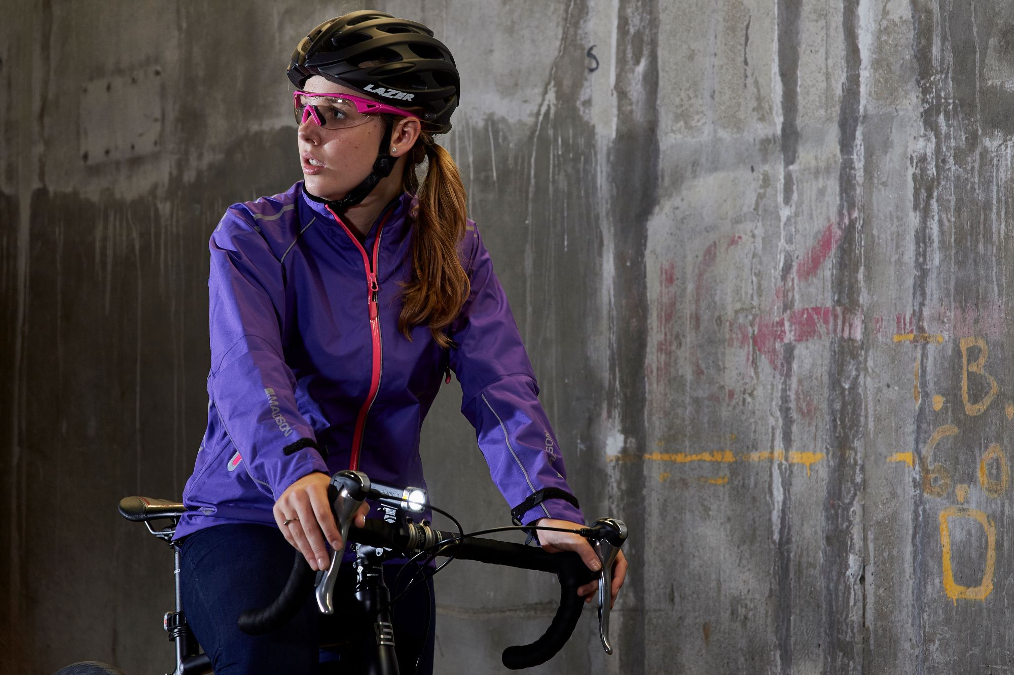 A woman on a bicycle wearing a purple Madison cycling jacket and black Lazer helmet