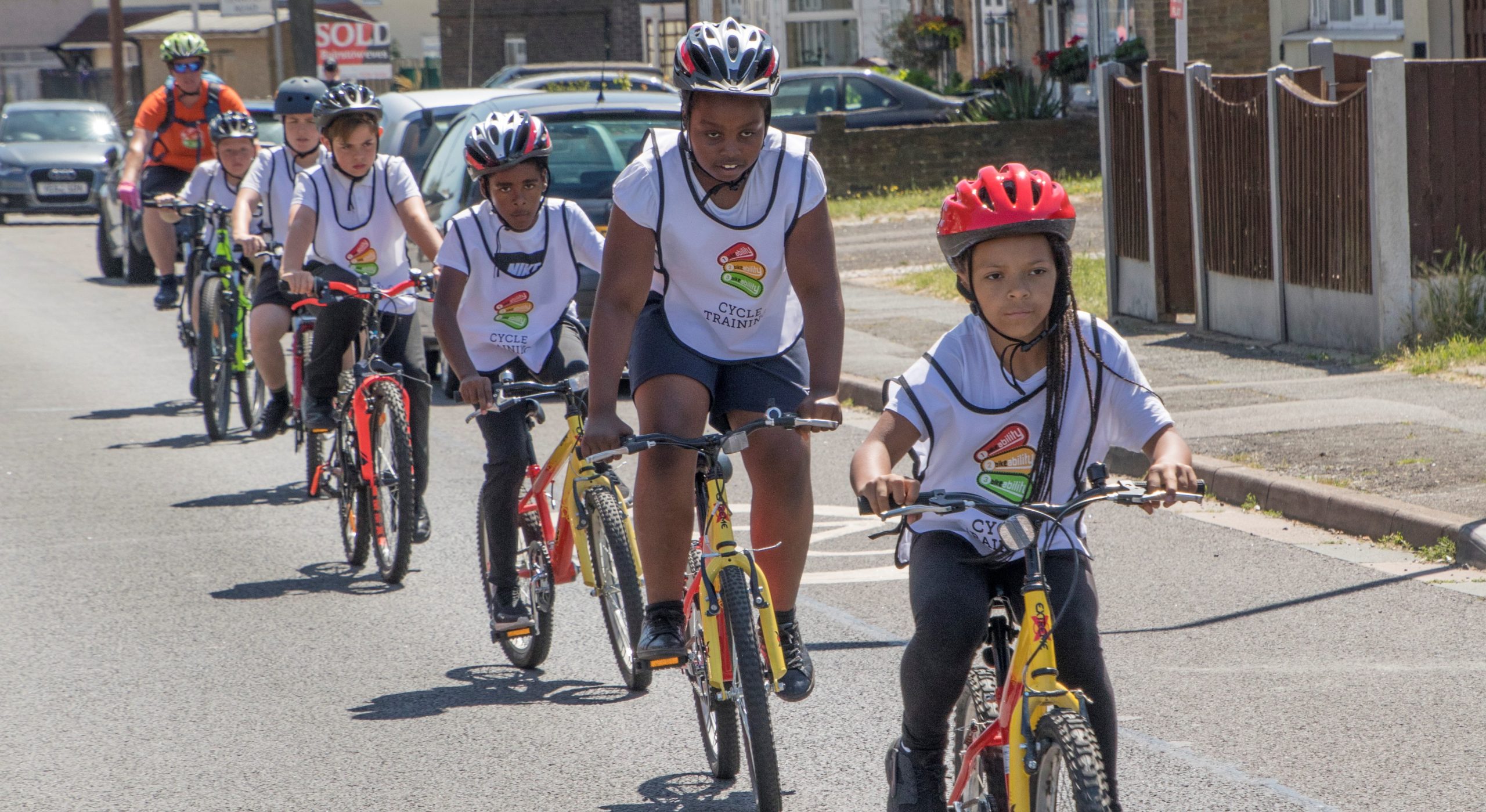 A group of children cycle in a line on the road during a Bikeability session.