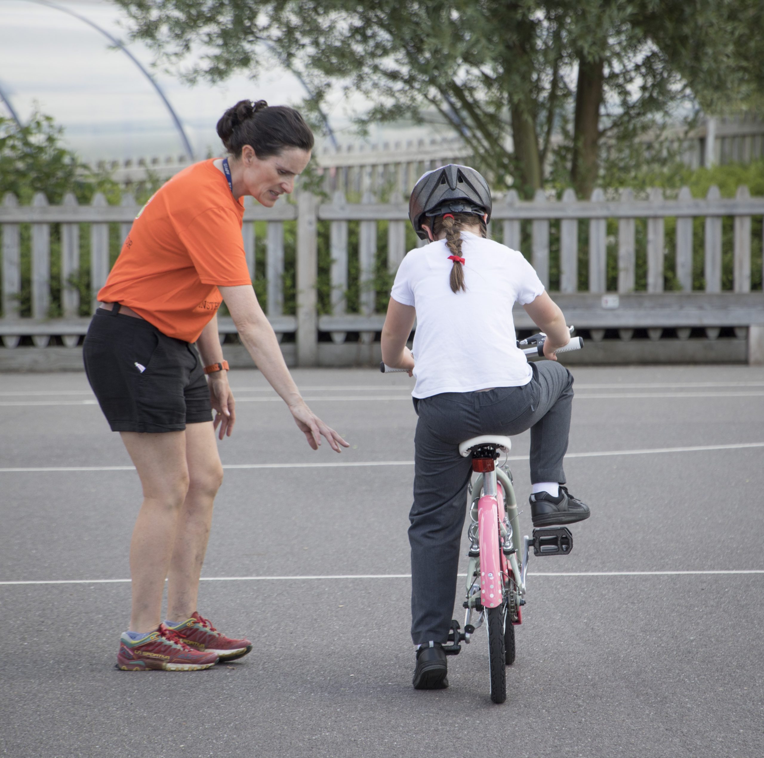 A bikeability instructor with a young girl on a bike on the playground