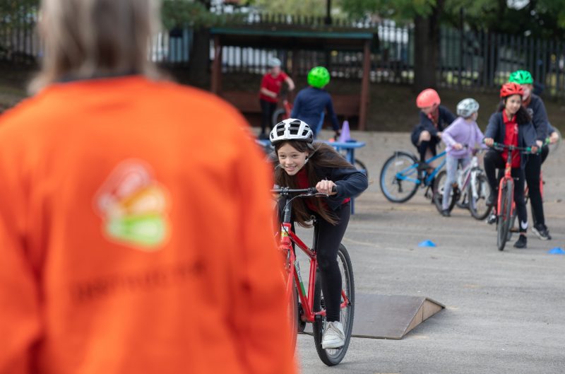 A Bikeability instructor watches a student testing out their skills in the playground