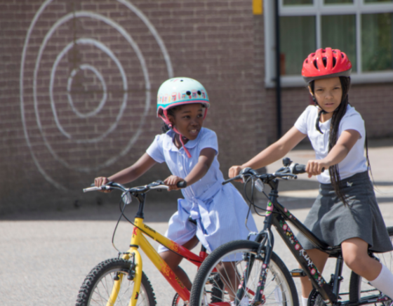 Two girls on bikes on the playground. Both wearing helmets and school uniform.