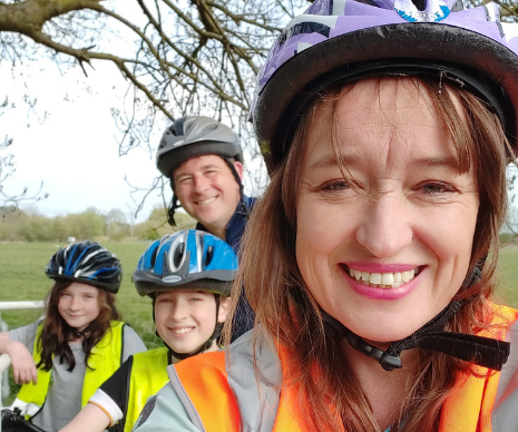 Emily Cherry wearing a cycle helmet in the foreground with her husband and two children wearing helmets in the background.