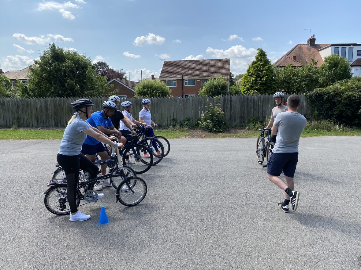 A group of people on bikes are on the left of the image, looking at a coach on the right.