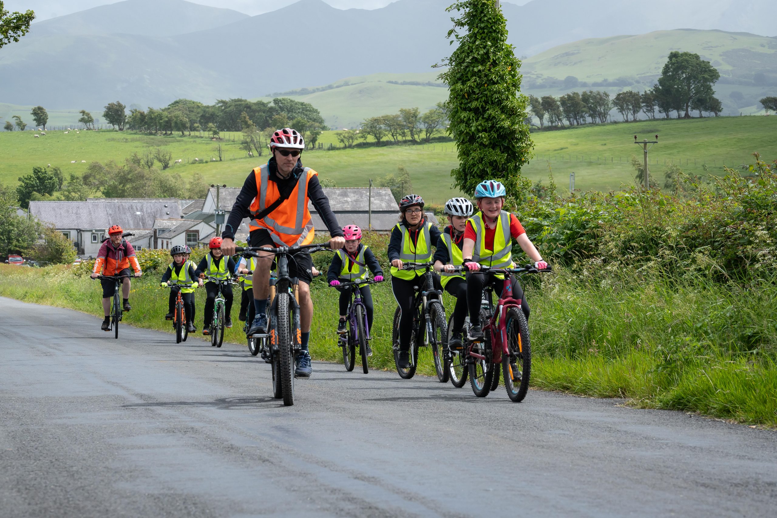 A group of children cycle single file towards the camera on a countrey