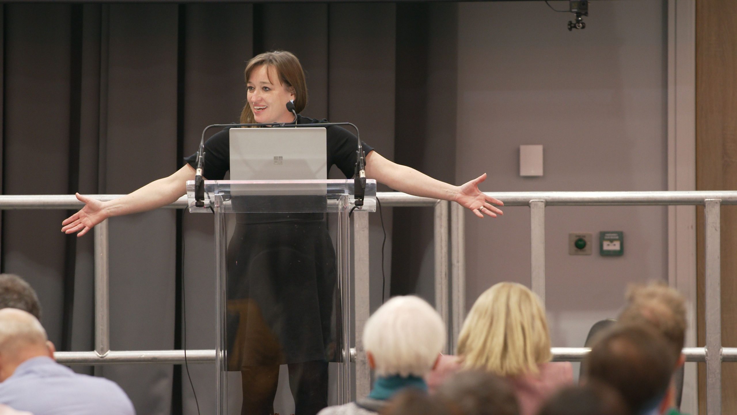Emily Cherry stands behind a lectern on stage, with her arms open wide