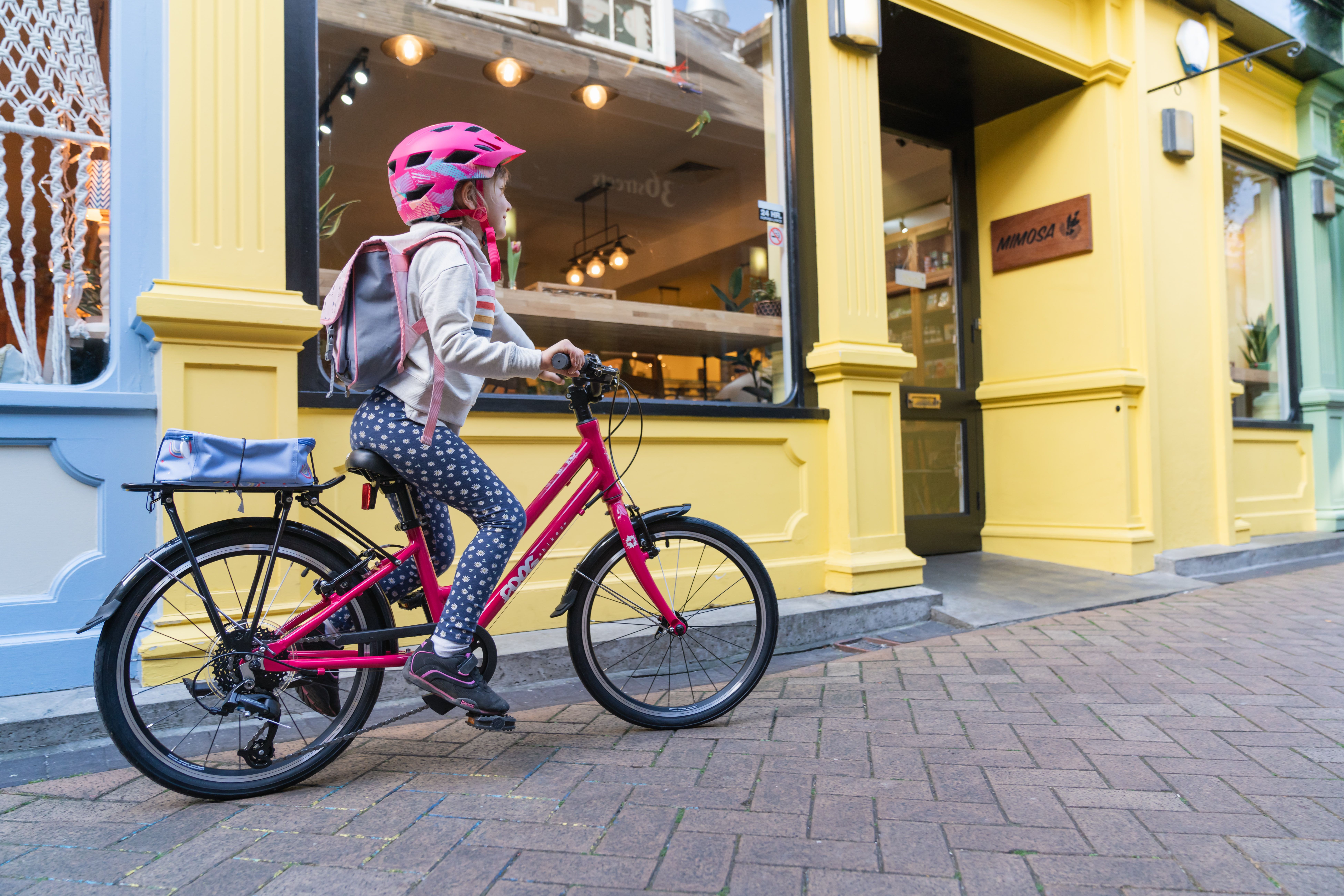 A young boy wearing denim shorts and a t shirt, plus a cycling helmet cycles along a suburban street on a blue Forme bike