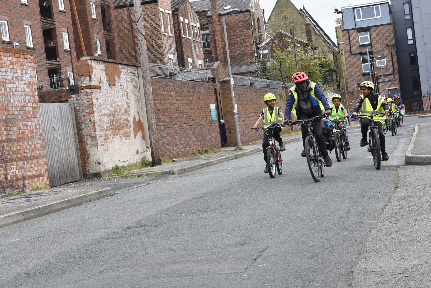 A man wearing a red cycle helmet and yellow high vis cycles ahead of a group of young boys riding bikes and wearing high vis vests.
