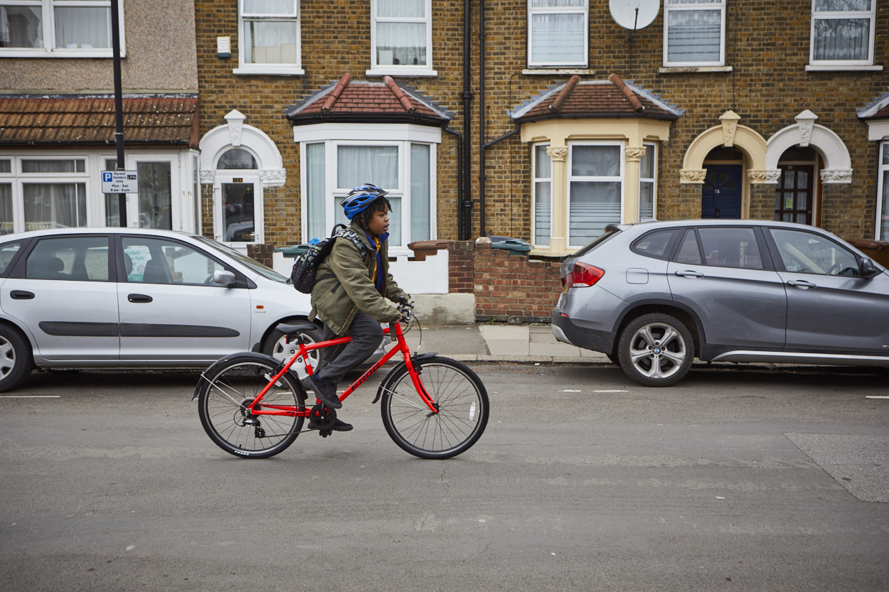 A boy wearing a green jacket and blue helmet cycles along a residential street on a red bike.