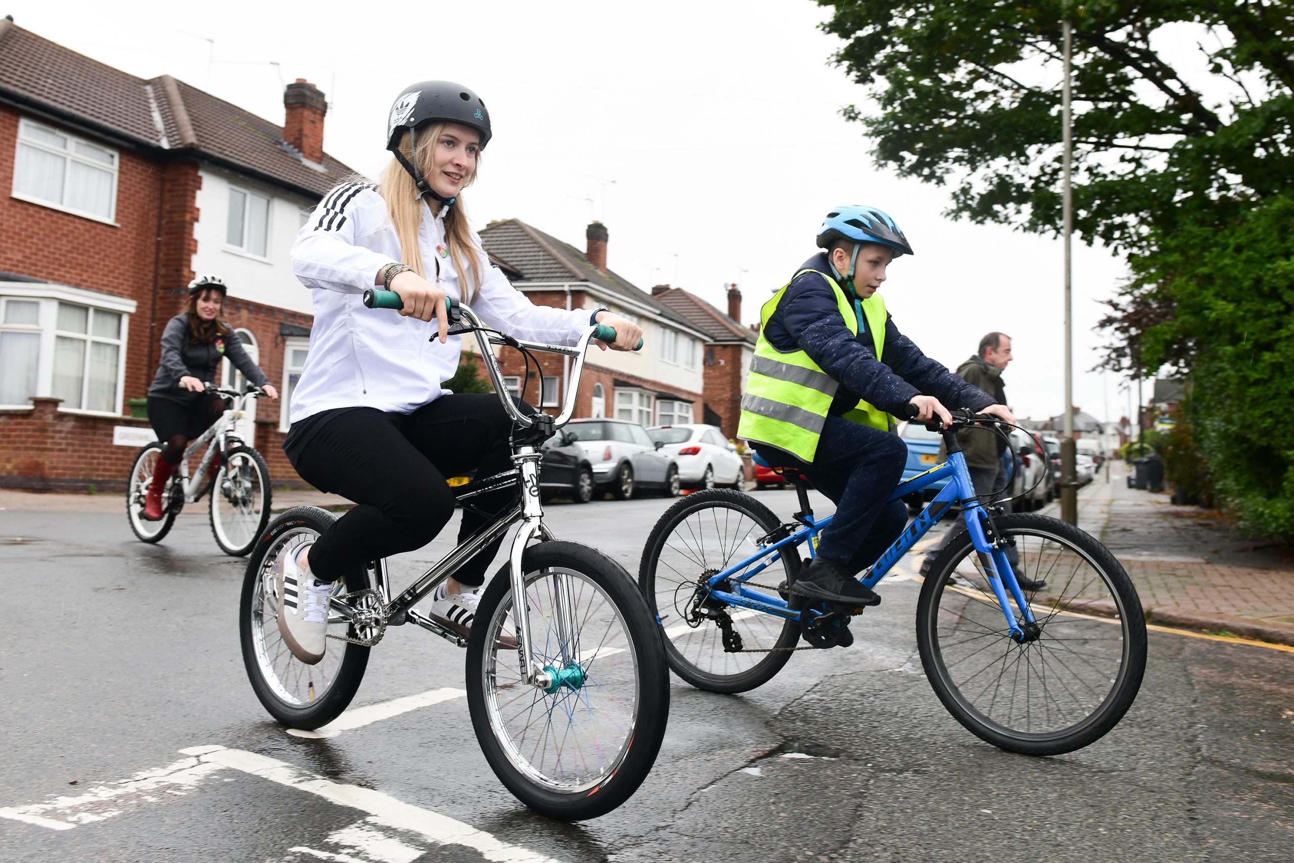 Charlotte Worthington is taking part in Bikeability cycle training. She is riding her bicycle in primary position next to a child on his bicycle. They are both wearing safety helmets.