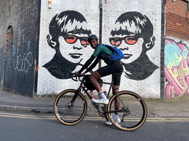 Varun on his bicycle in front of a wall with graffiti