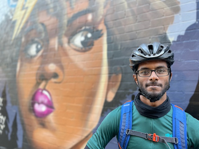 Cyclist Varun wearing a cycle helmet standing in front of some graffiti