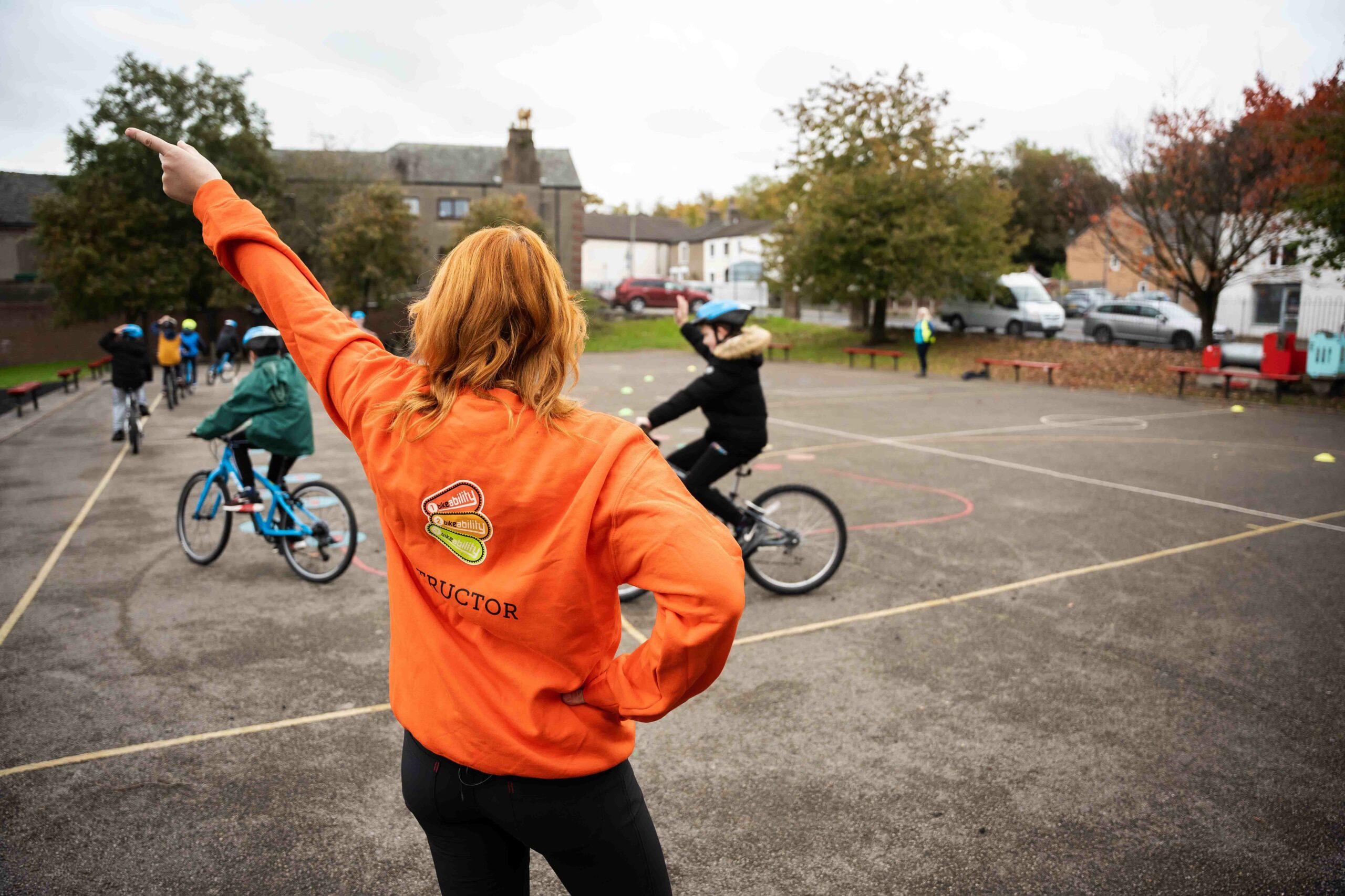 Instructor delivering Bikeability lesson while children cycle around the playground