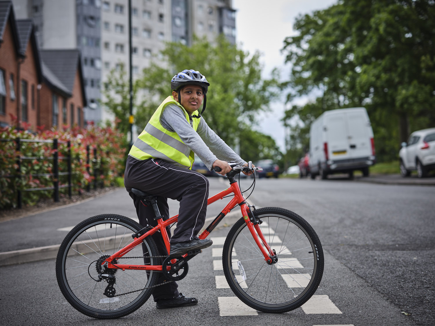 A young Bikeability trainee is sitting on their bicycle in primary position at a junction. They are looking confidently to their right towards the camera.