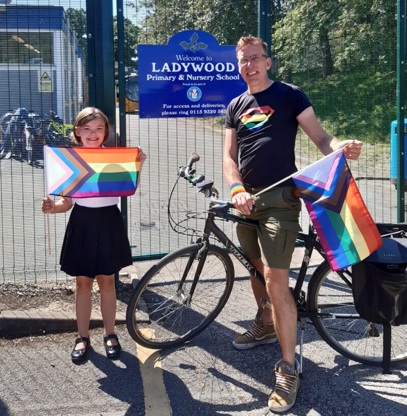 Rob delivering Pride flags standing with a bike and smiling