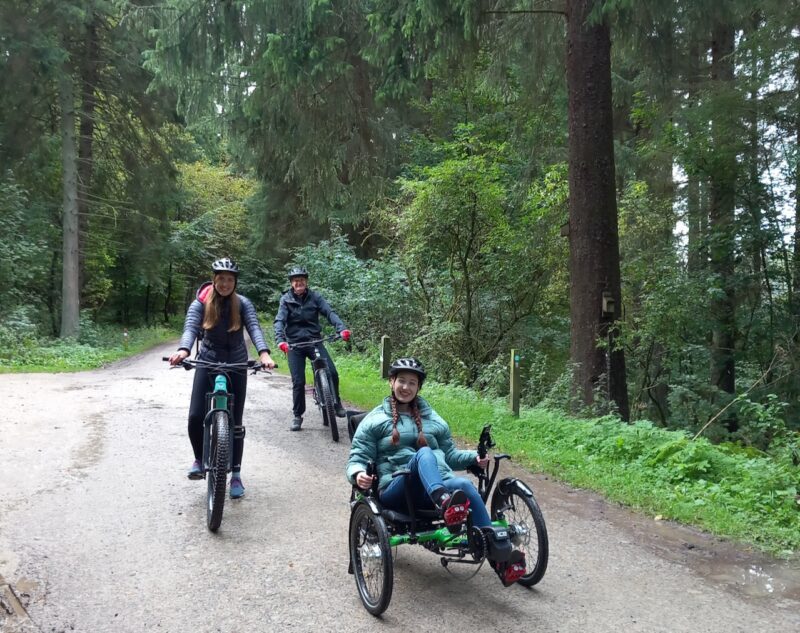 Three people cycling in the forest with different types of cycles including an recumbent trike