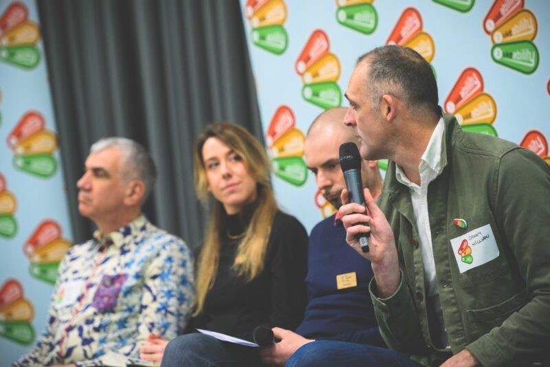 Speakers at the Bikeability conference in 2023. One is leaning forward and talking on a microphone