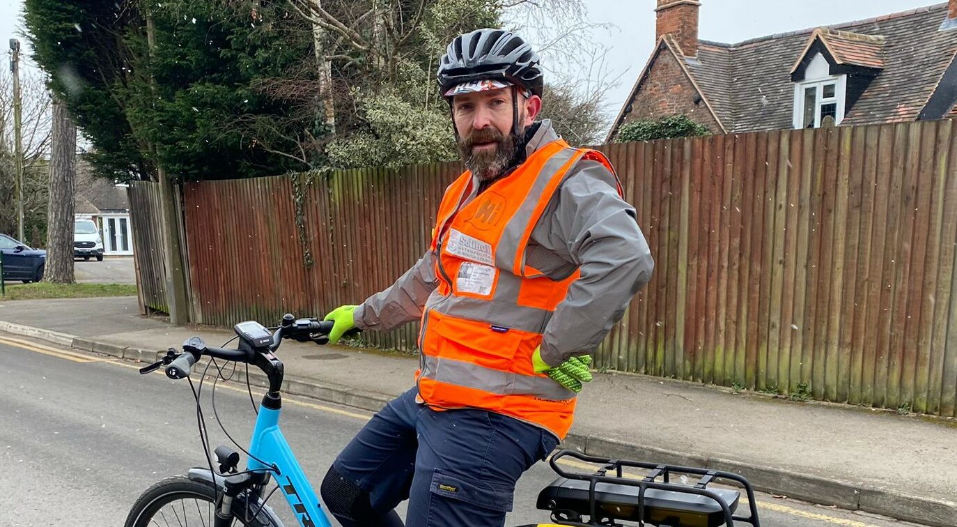 Instructor Perry with his blue bicycle he is wearing hi vis, a helmet and smiling at the camera