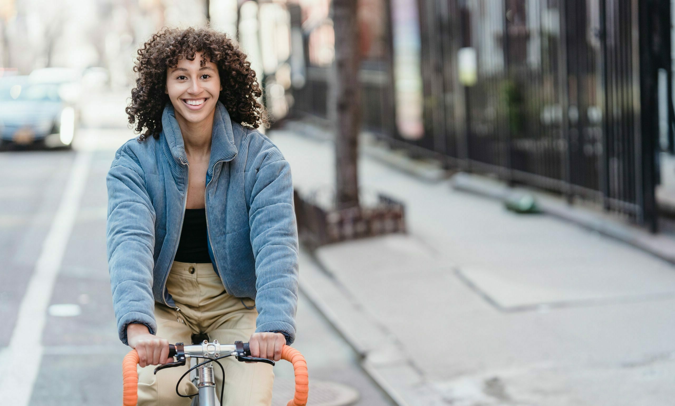 A smiling woman in a blue coat riding a cycle with orange handlebars