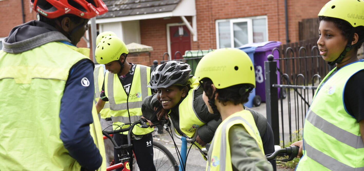 A group of students are taking part in a Bikeability lesson. One is doing a big cheeky grin straight at the camera