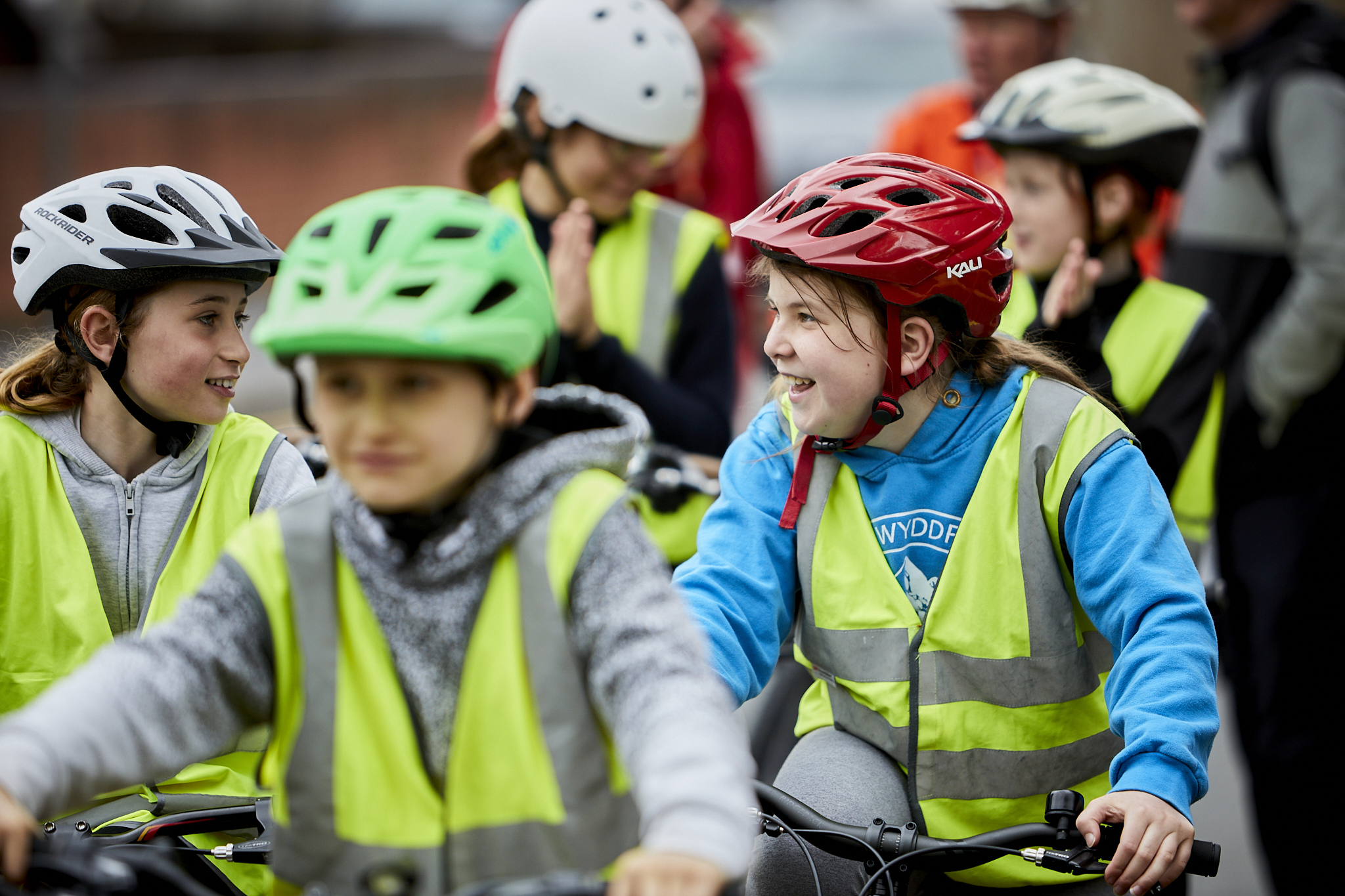 Two girls, wearing helmets and high vis, laugh in a group of cyclists as they take part in Bikeability training