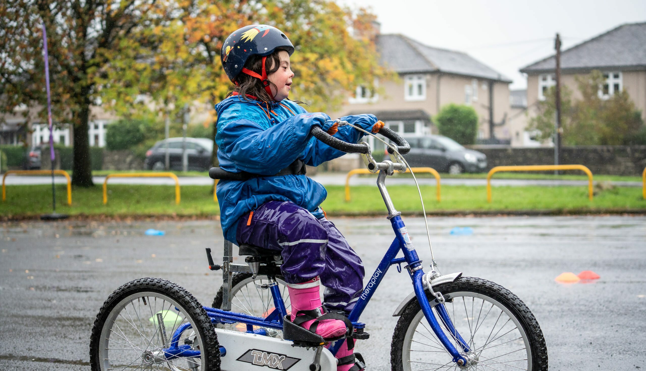 A Bikeability student riding a tricycle. They are wearing a blue coat and a helmet with star stickers on it.