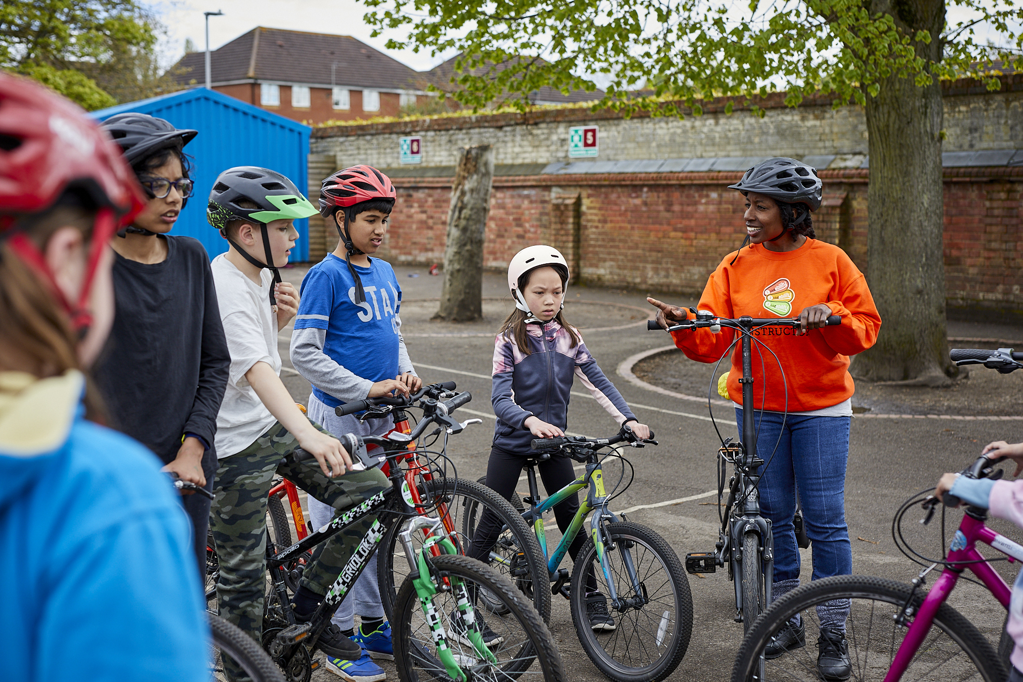 A Bikeability instructor is talking to a group of students. They are all sitting on their cycles.