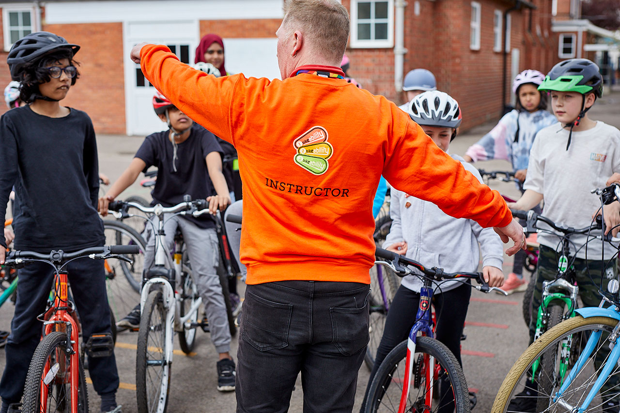A Bikeability instructor giving directions to a group of riders in a playground