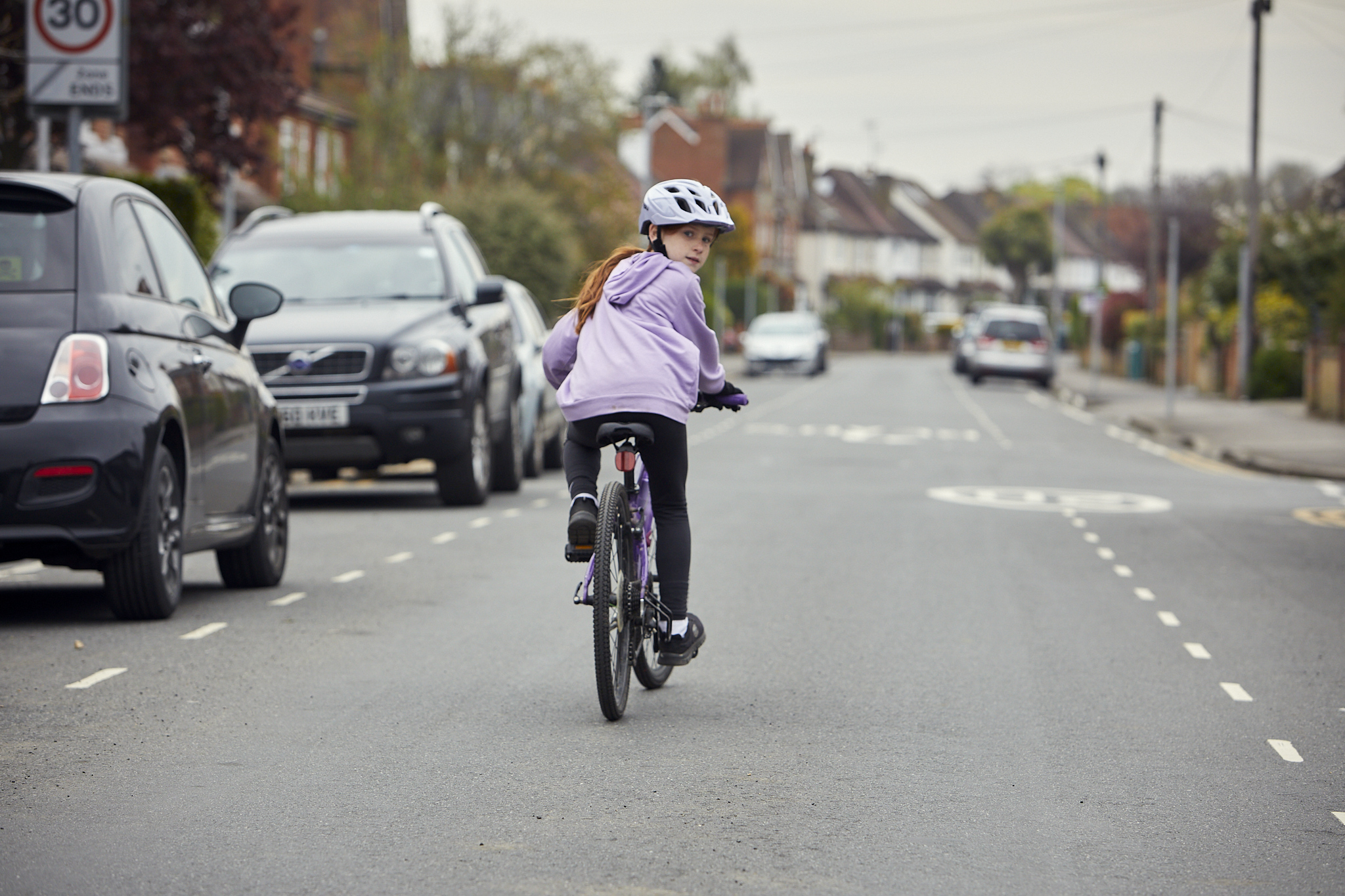 A young girl cycles on the road. She is looking over her shoulder to check before she changes position