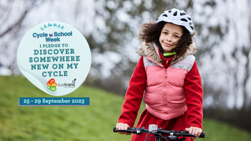 A girl on her cycle in a park. There is a sticker on top saying I pledge to discover somewhere new on my cycle