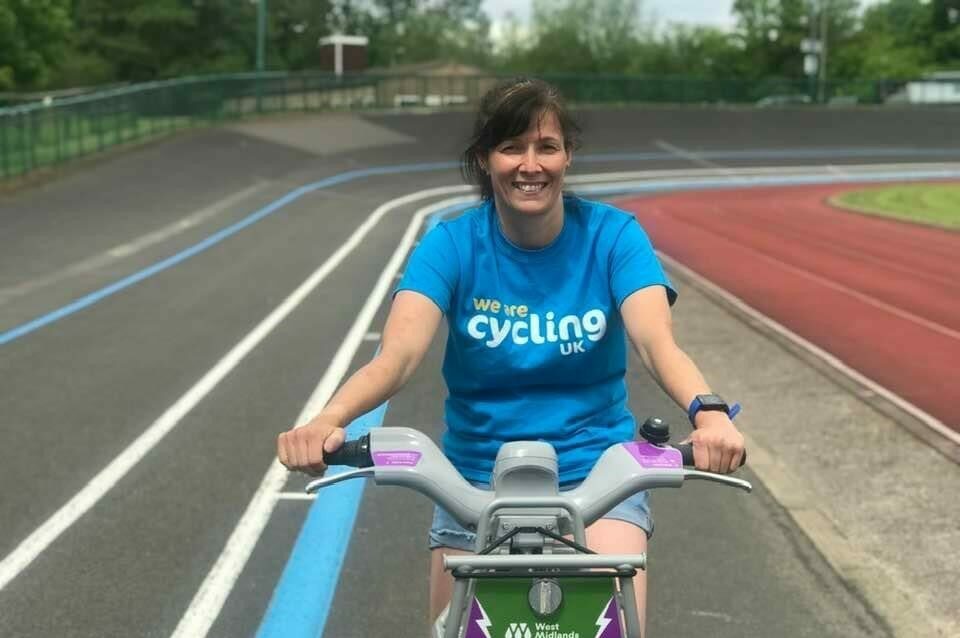 Michelle sitting on a hire bike. She is wearing a blue t shirt that says Cycling UK on it and smiling