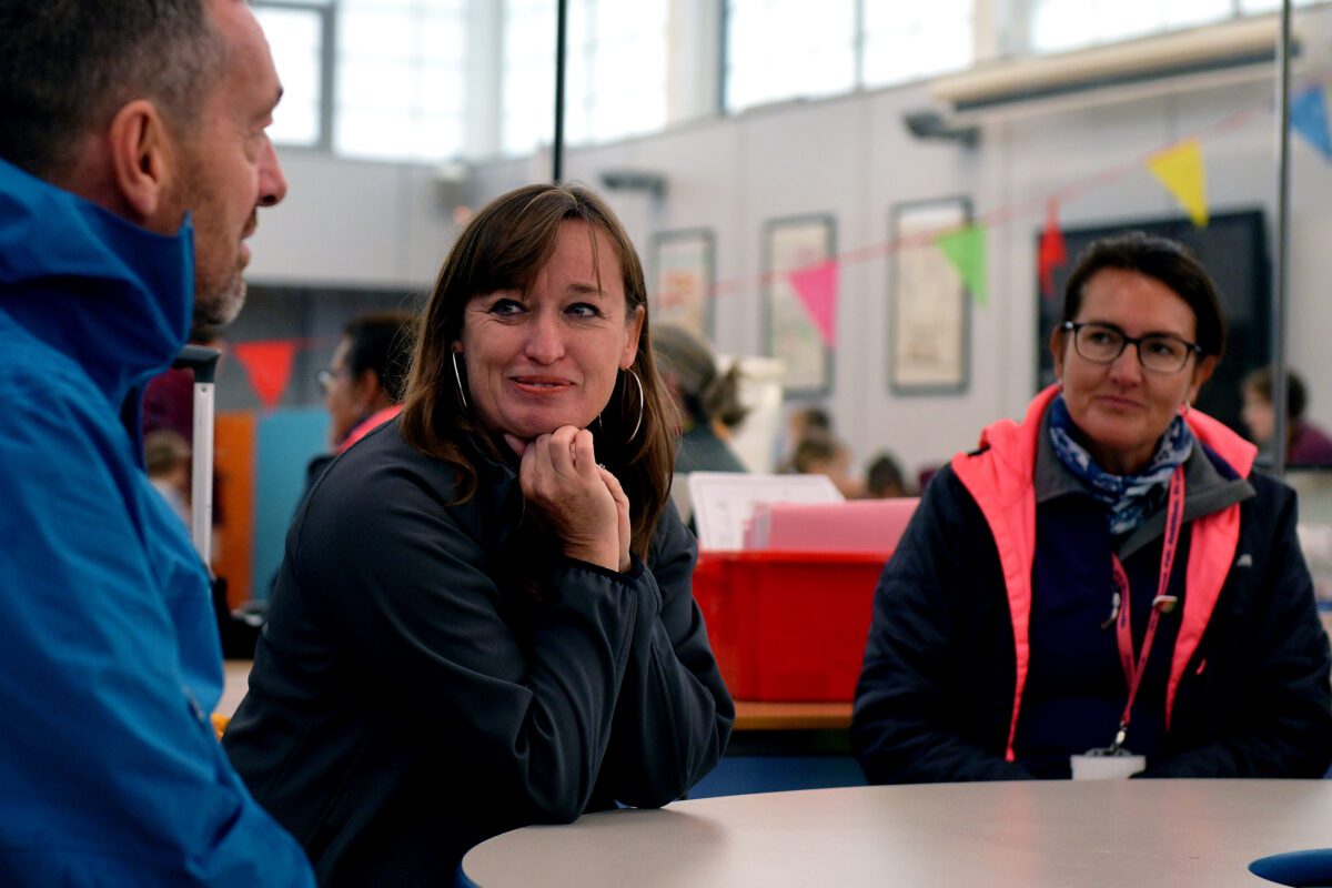 Emily Cherry is sitting in a school canteen with Chris Boardman and a Bikeability instructor.