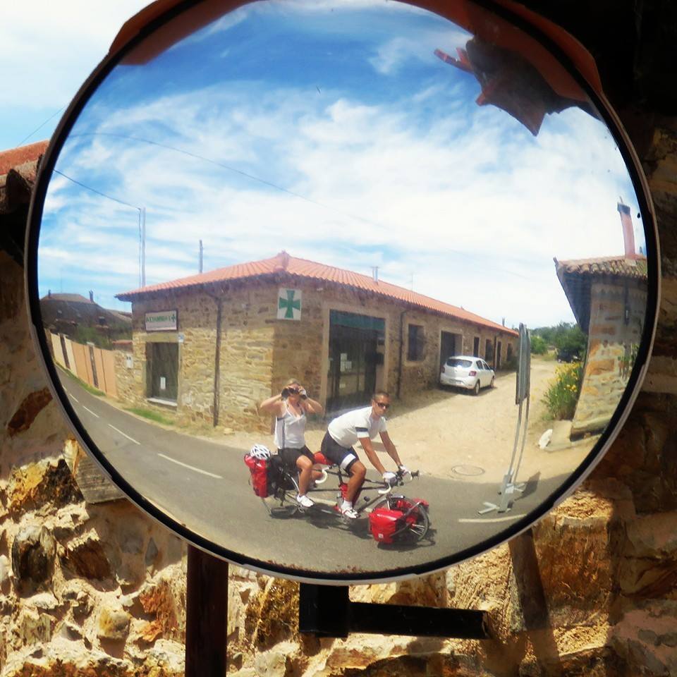 Rosie and her tandem partner on a tandem cycle. The photo is taken as a reflection in a round roadside mirror as they cycle past
