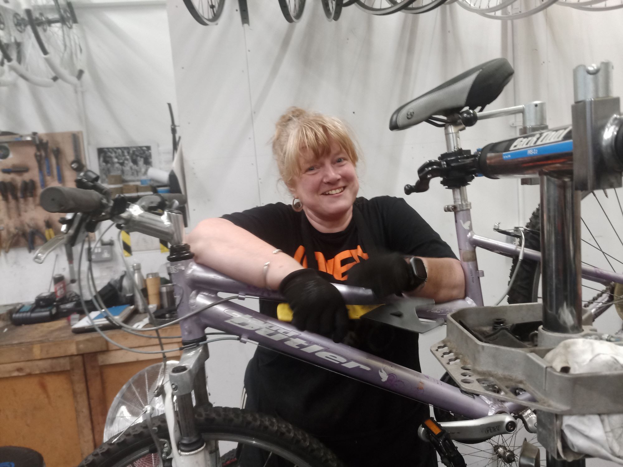 Cath Palgrave standing being a bicycle on a stand that she is fixing. She has a big smile