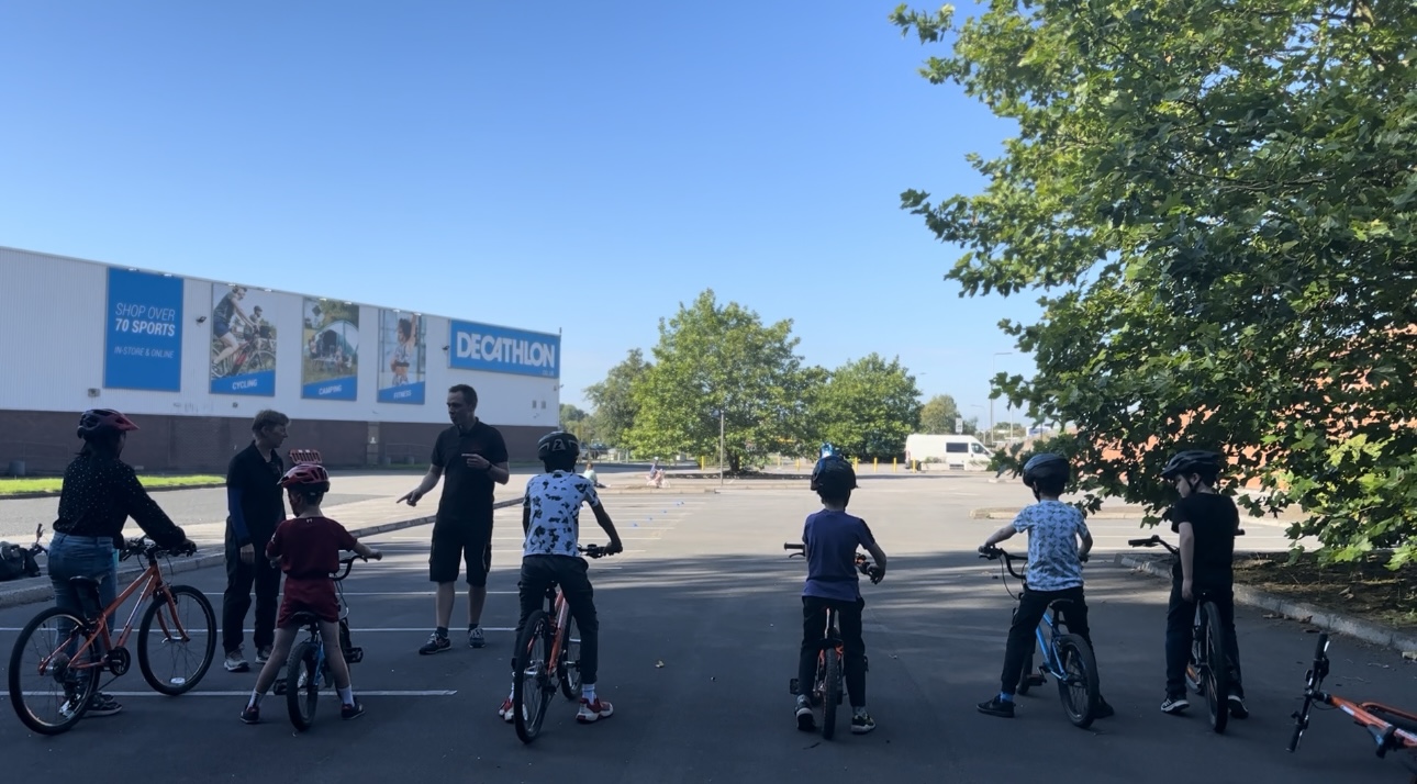 A group of Bikeability riders are getting instruction in a Decathlon store car park