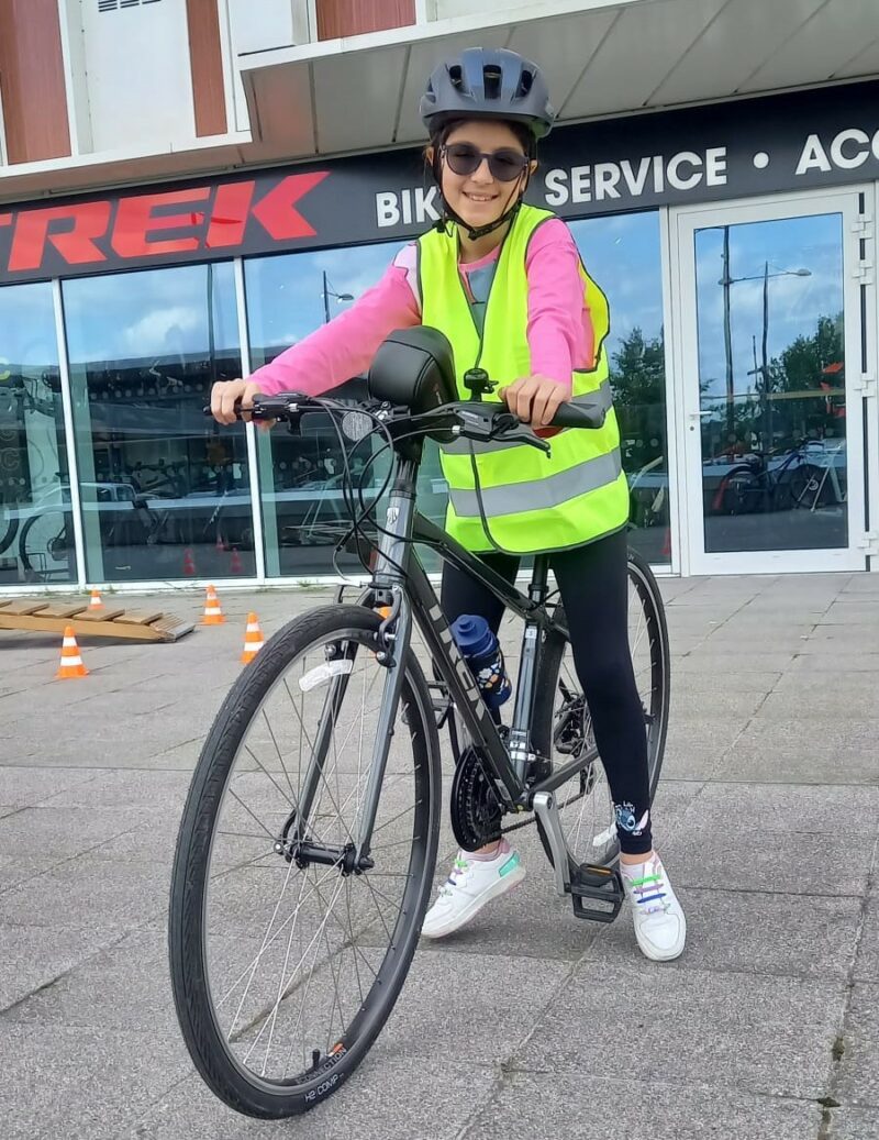 Anastasia on her bike. She is wearing a hi vis vest over a pink jumper and smiling