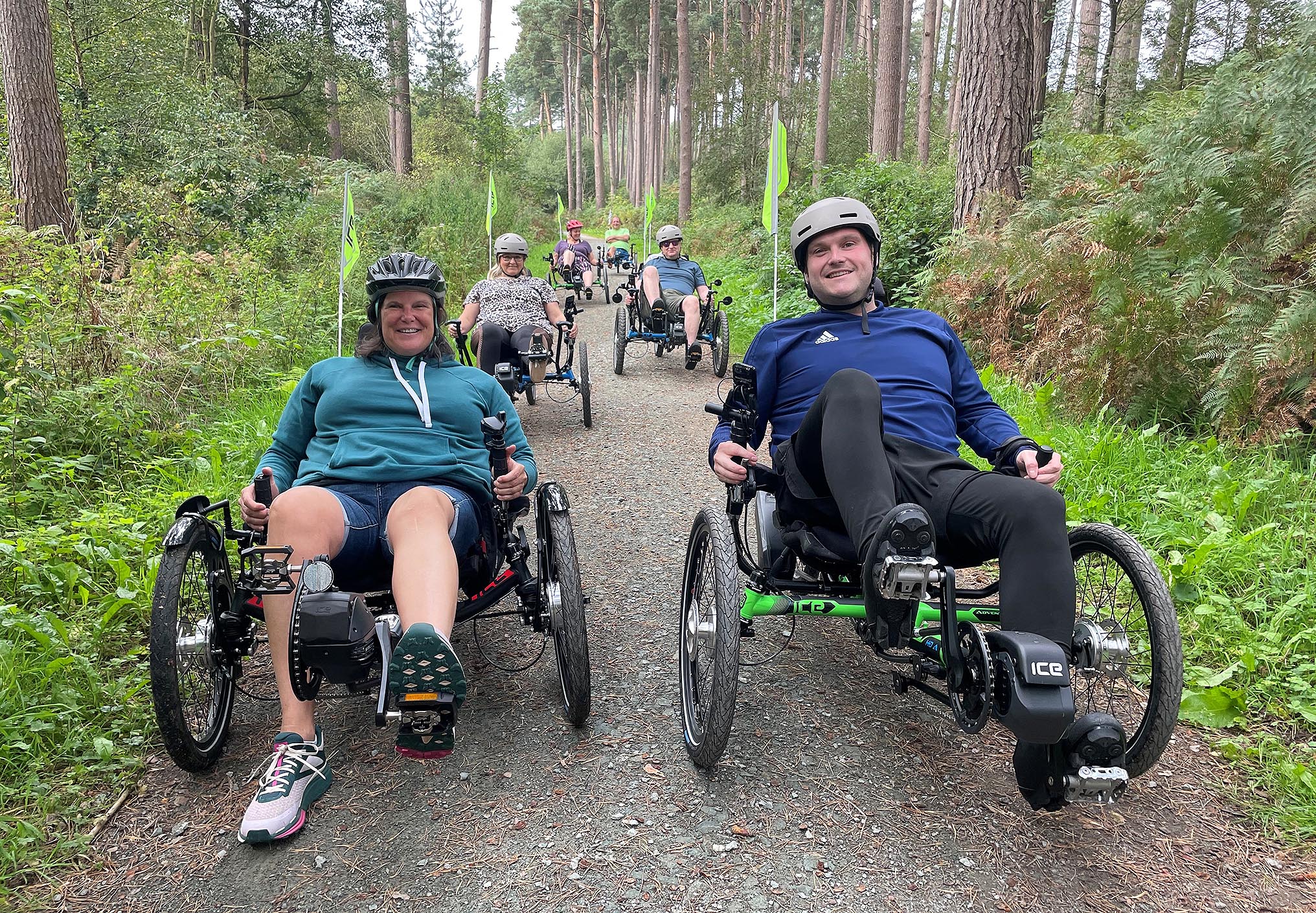 A group of people cycle through a forest on a range of ICE Trike recumbent tricycles.