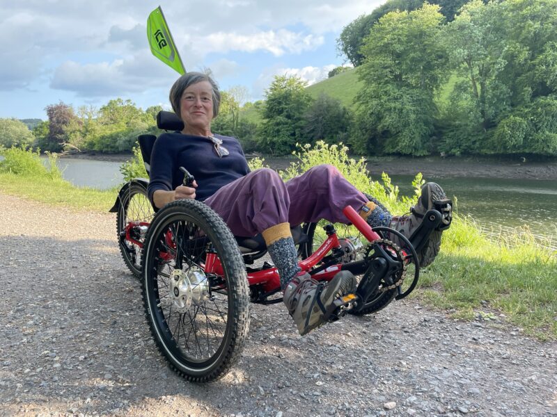 Holly is riding her ICE Trike on a sunny riverside path in the countryside.
